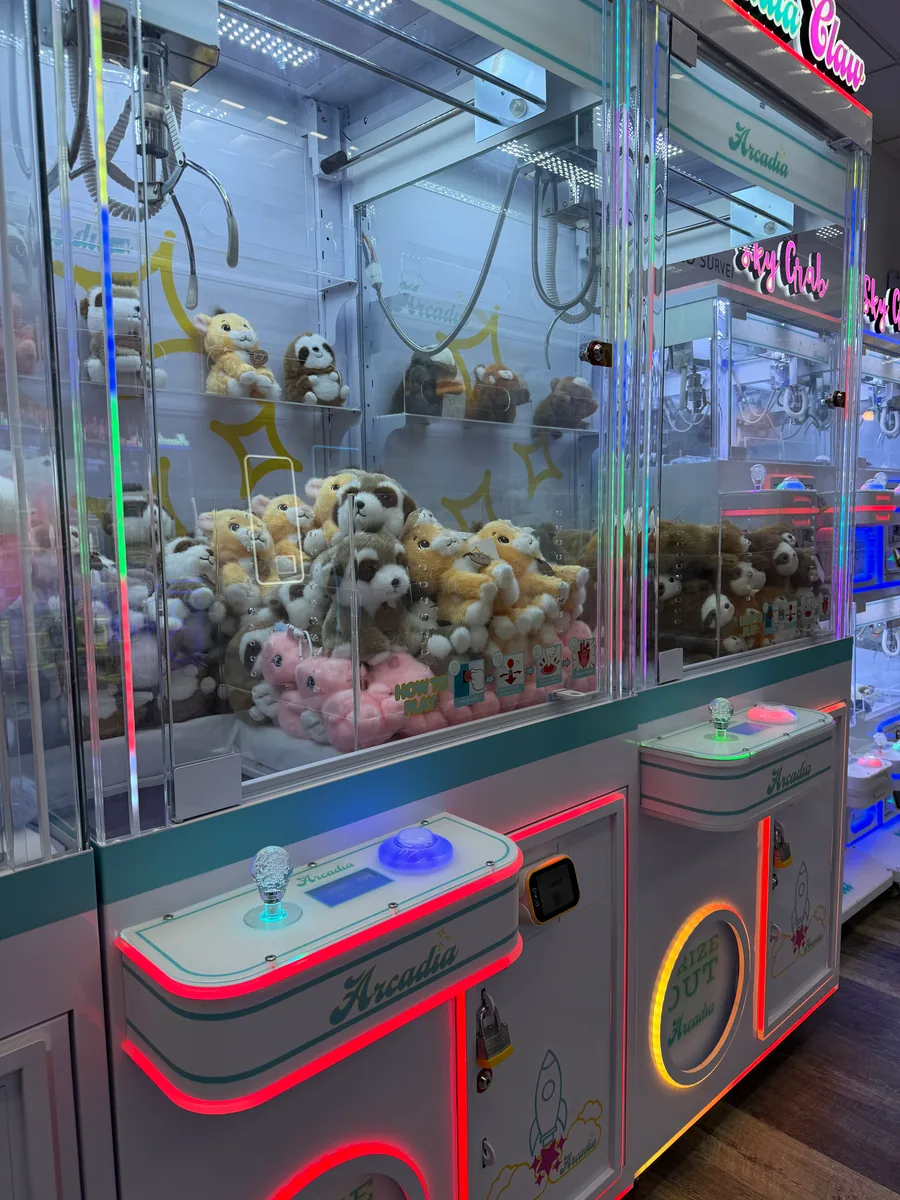 Plush-filled Arcadia claw machines with illuminated controls and visible claw mechanisms