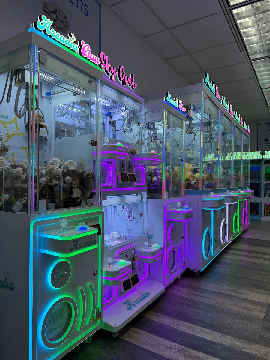 A coordinated row of Arcadia claw machines with illuminated controls and plush prizes