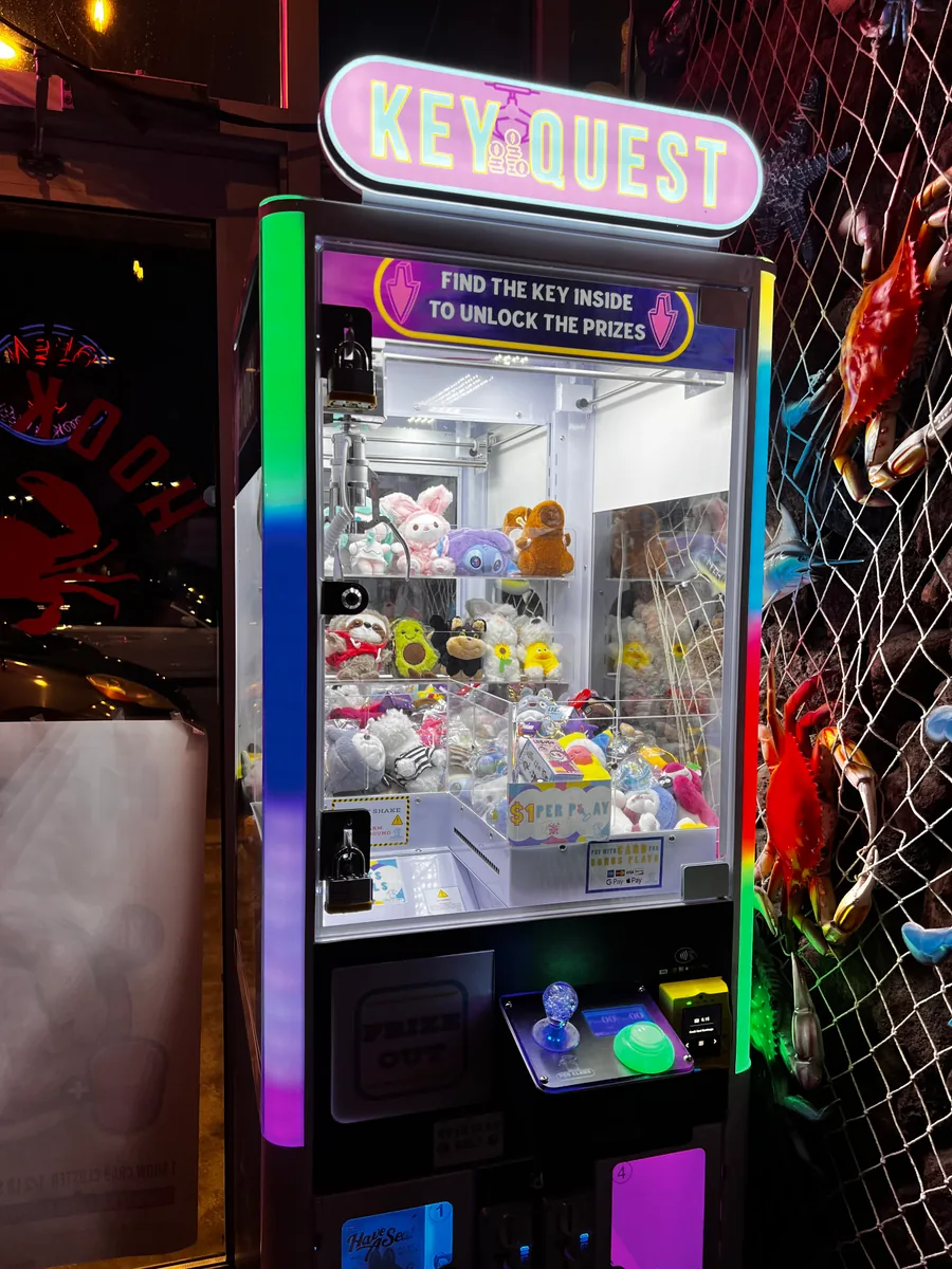 A real Key Quest machine with its illuminated topper, plush prizes, and card reader at a venue