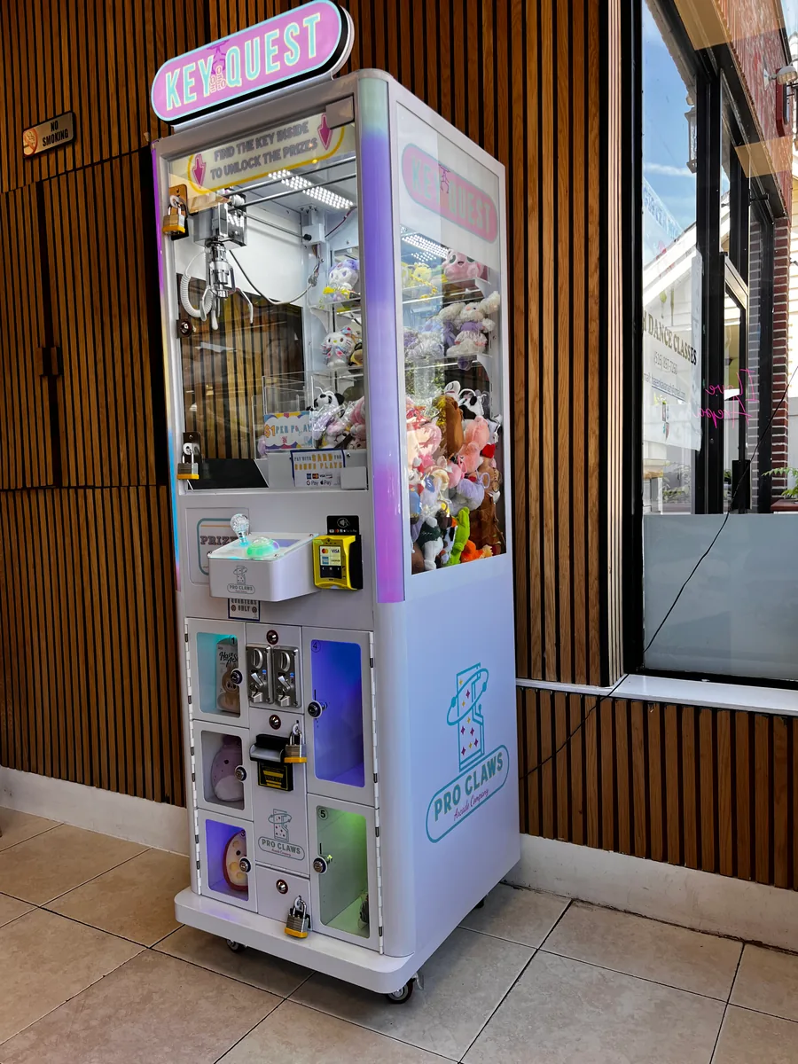 A white Pro Claws Key Quest cabinet combining a plush claw game and numbered prize lockers