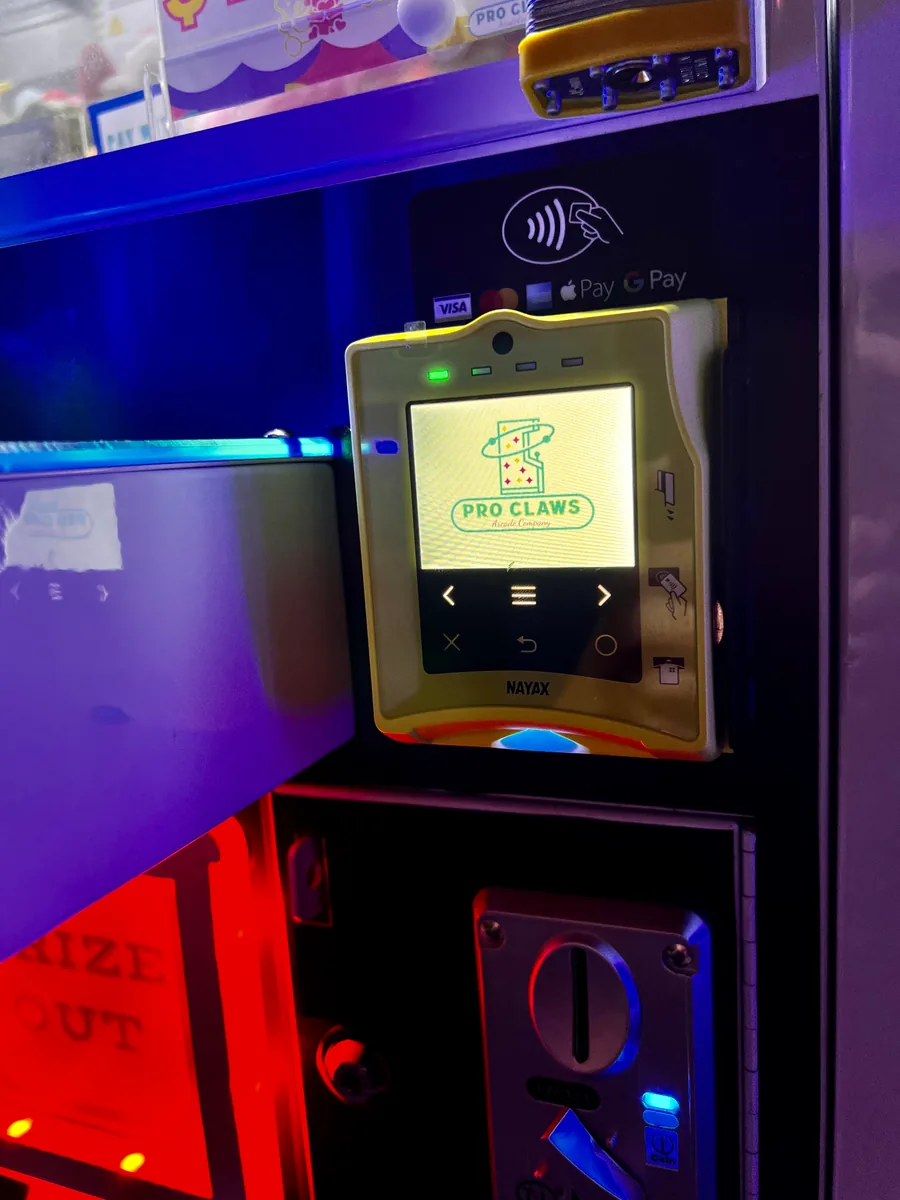 A real Pro Claws machine with a Nayax reader displaying our logo, card and mobile wallet marks, and a coin slot below