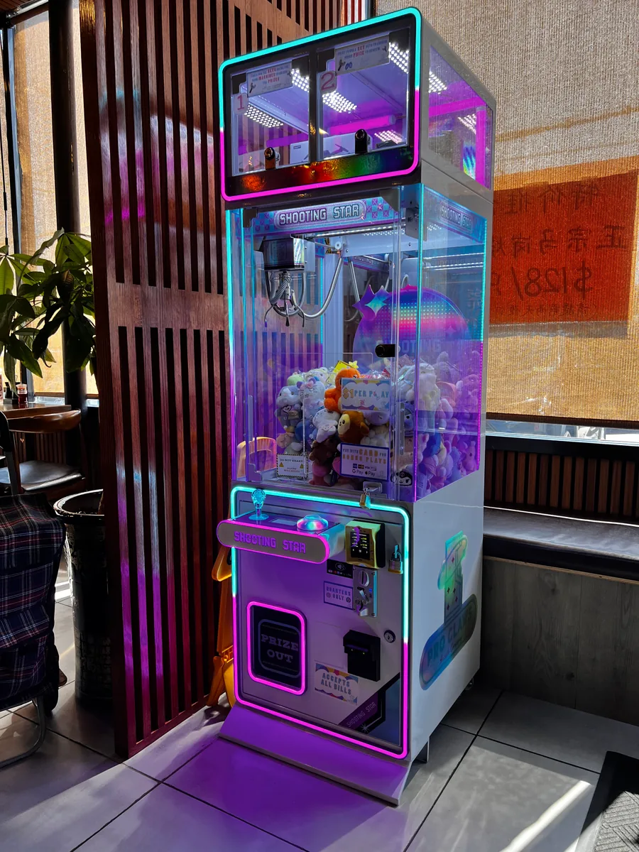 A Shooting Star claw machine filled with plush toys, photographed from the side beside restaurant seating